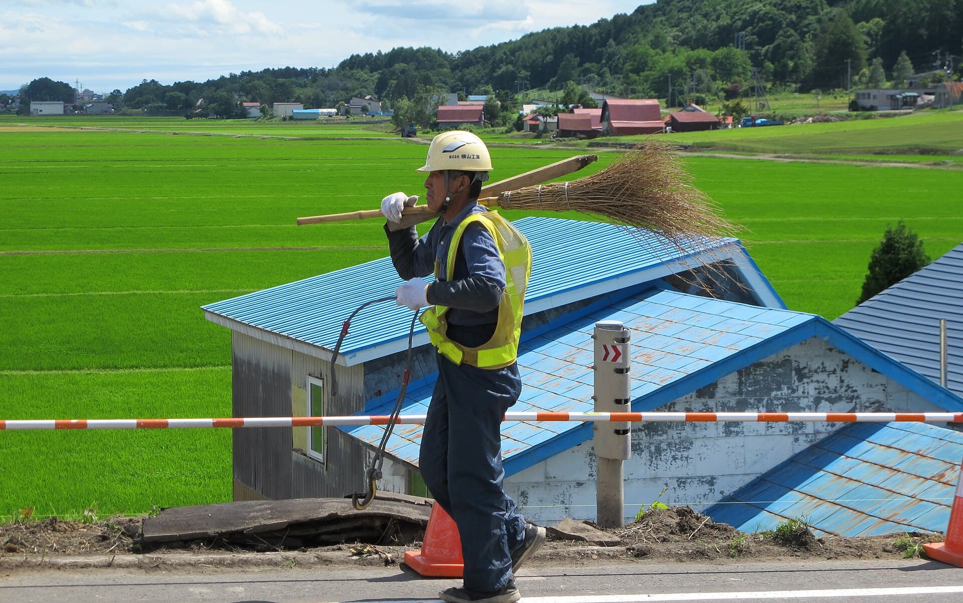 A worker in a high-visibility vest carrying gear across a rural bridge
